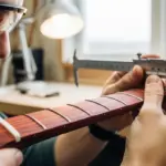Un luthier examine attentivement un manche de guitare en bois de sang dans un atelier bien éclairé.